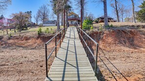A wooden bridge leading to a house with a balcony, surrounded by trees and a clear sky. - Classic Lake O' the Pines Retreat! Dock, Fire Pit (Jefferson)