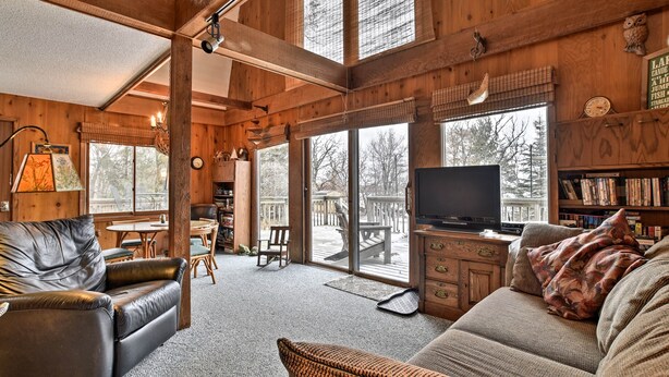 A cozy cabin interior with a leather sofa, a television, and a wooden bookshelf.
