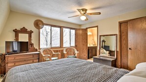 A bedroom with a large bed, wooden furniture, a ceiling fan, and a window with a view of trees.