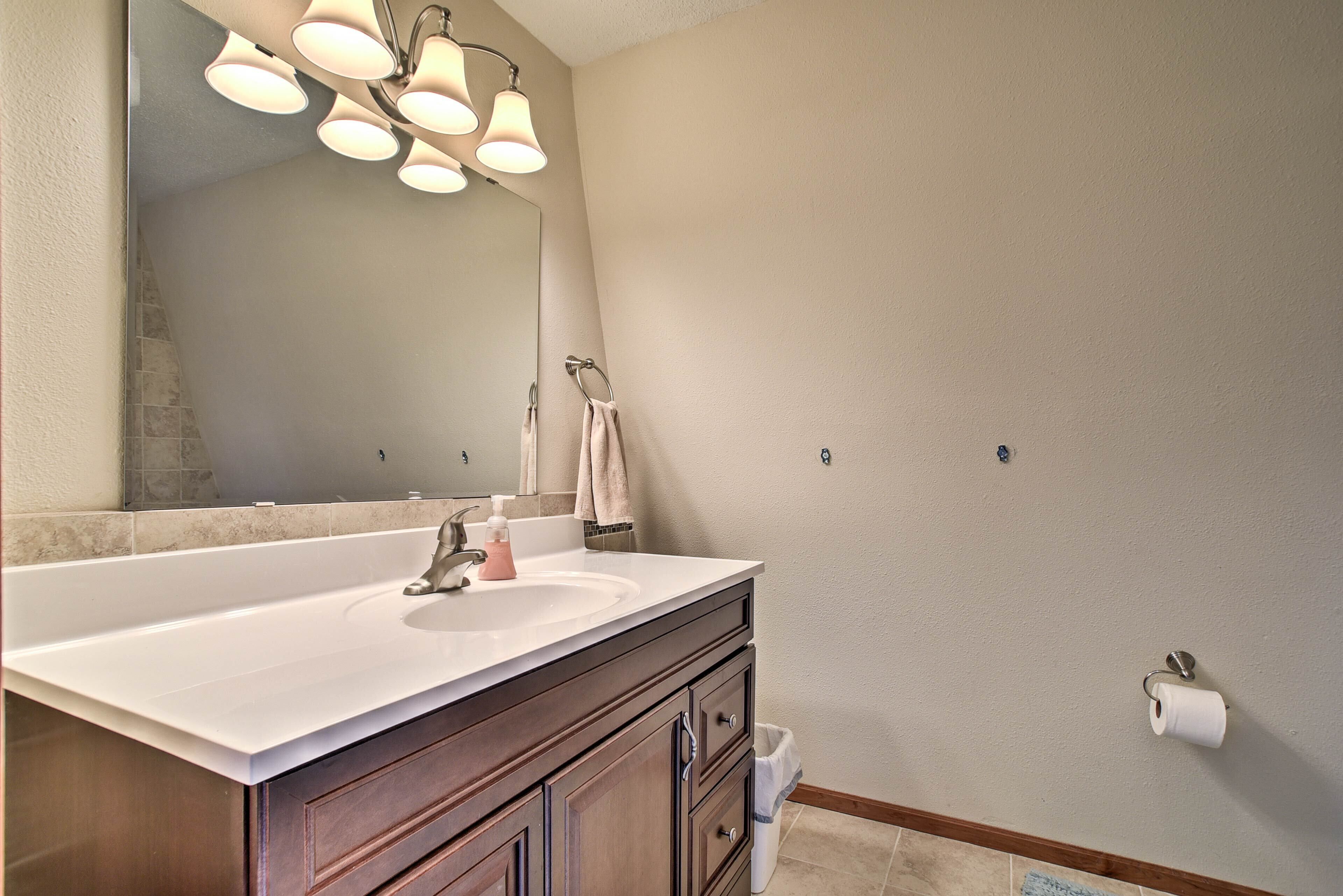Une salle de bain avec un grand lavabo blanc, un meuble-lavabo en bois foncé, un miroir et un porte-rouleau de papier toilette fixé au mur.