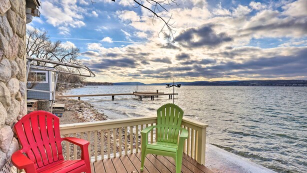 Une terrasse en bois avec deux fauteuils Adirondack, un mur de pierres et une vue sur un lac et des montagnes lointaines.