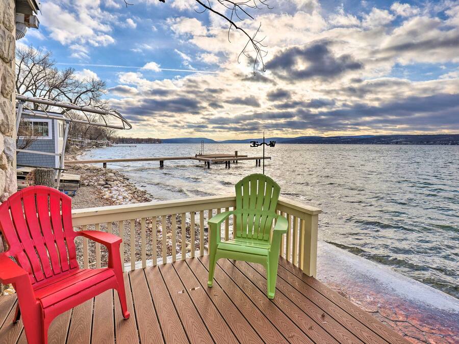 Una terraza de madera con dos sillas Adirondack, un muro de piedra y vistas a un lago y montañas distantes.