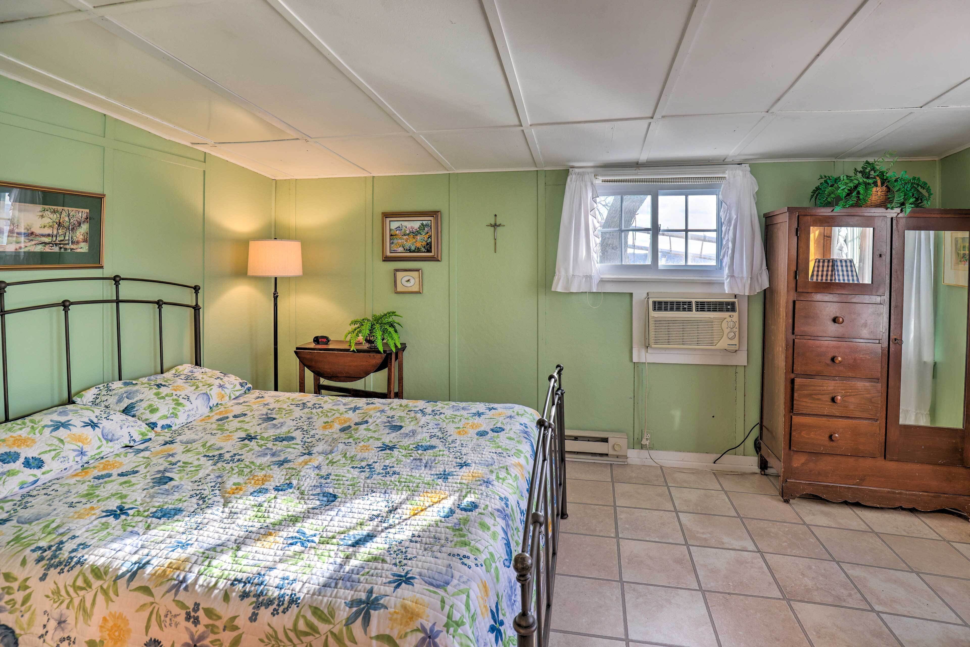 Une chambre à coucher comprenant un lit, une commode, une fenêtre avec un rideau, une lampe et un climatiseur fixé au mur.