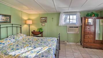 Une chambre à coucher comprenant un lit, une commode, une fenêtre avec un rideau, une lampe et un climatiseur fixé au mur.