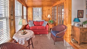 L’intérieur d’un chalet accueillant, avec un canapé rouge, des fauteuils en osier, une petite table avec une lampe et des murs en bois.