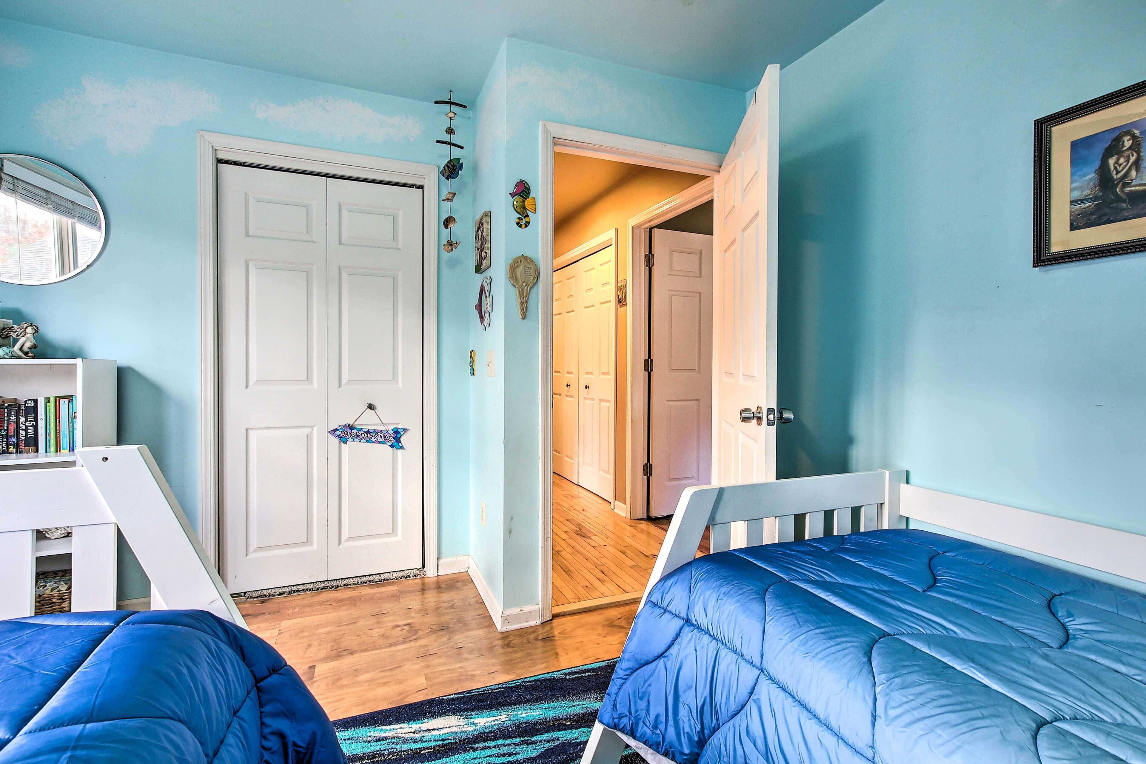 Quarto com duas camas, uma porta branca e um corredor que leva a outro espaço.