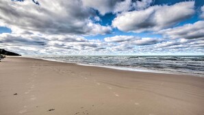 Une plage où l’on voit des empreintes de pas menant à l’eau, un ciel dégagé et une mer calme.