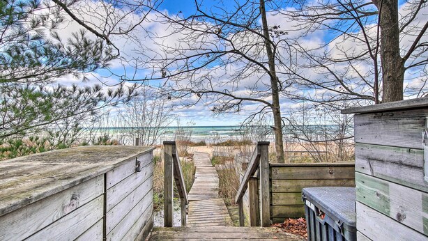 Un sentier en bois mène à une plage, bordé d’une clôture en bois d’un côté et d’une poubelle de l’autre.