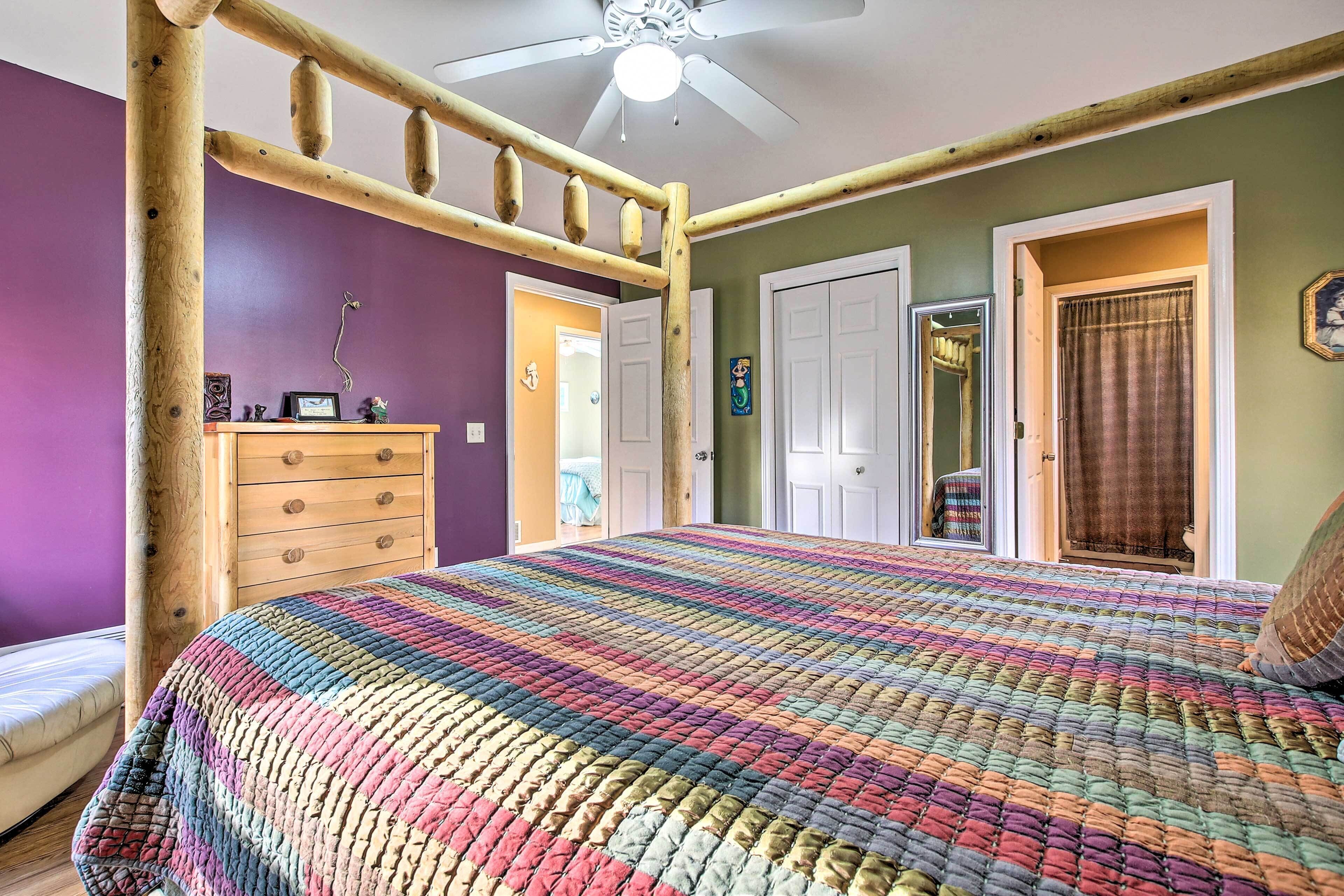 A bedroom with a colorful quilted bedspread, a wooden headboard, a ceiling fan, and a dresser with drawers.