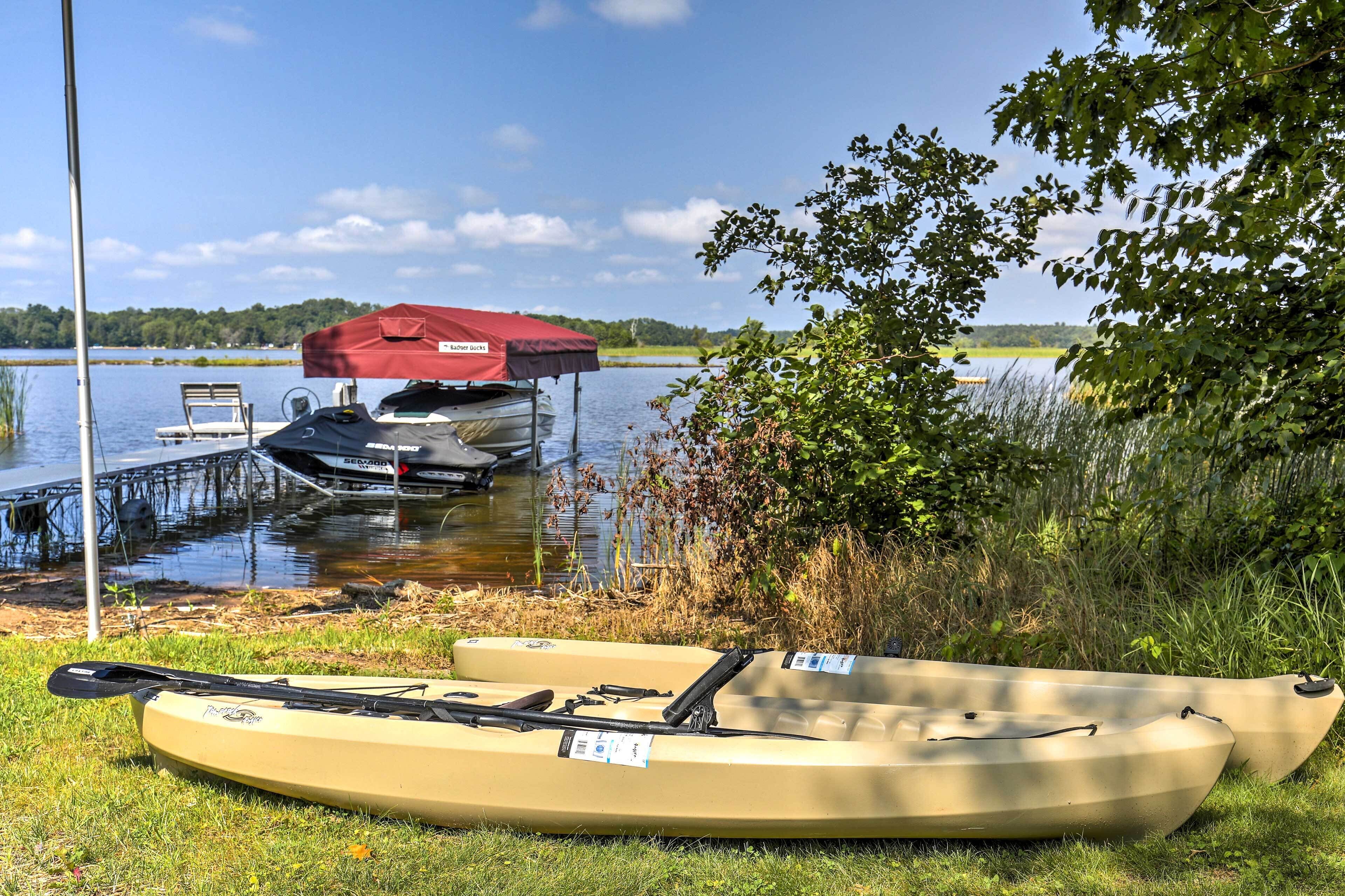 A kayak and canoe on grass near a dock with boats in the background.