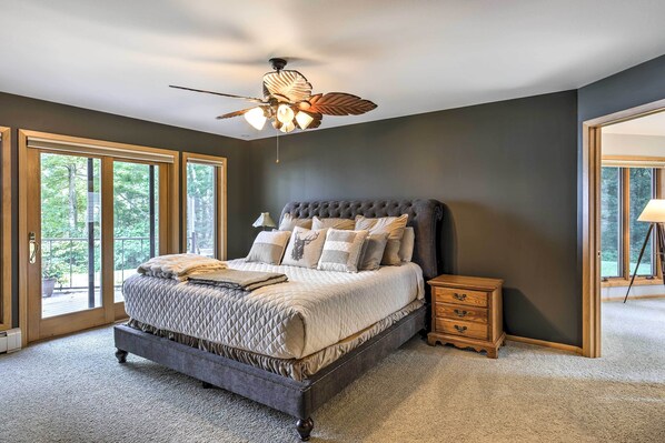 A bedroom with a large bed, a ceiling fan, and a view through the glass doors.