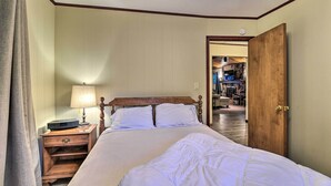 Habitación de hotel con una cama de madera, una mesita de noche con lámpara y una puerta que da a un pasillo.