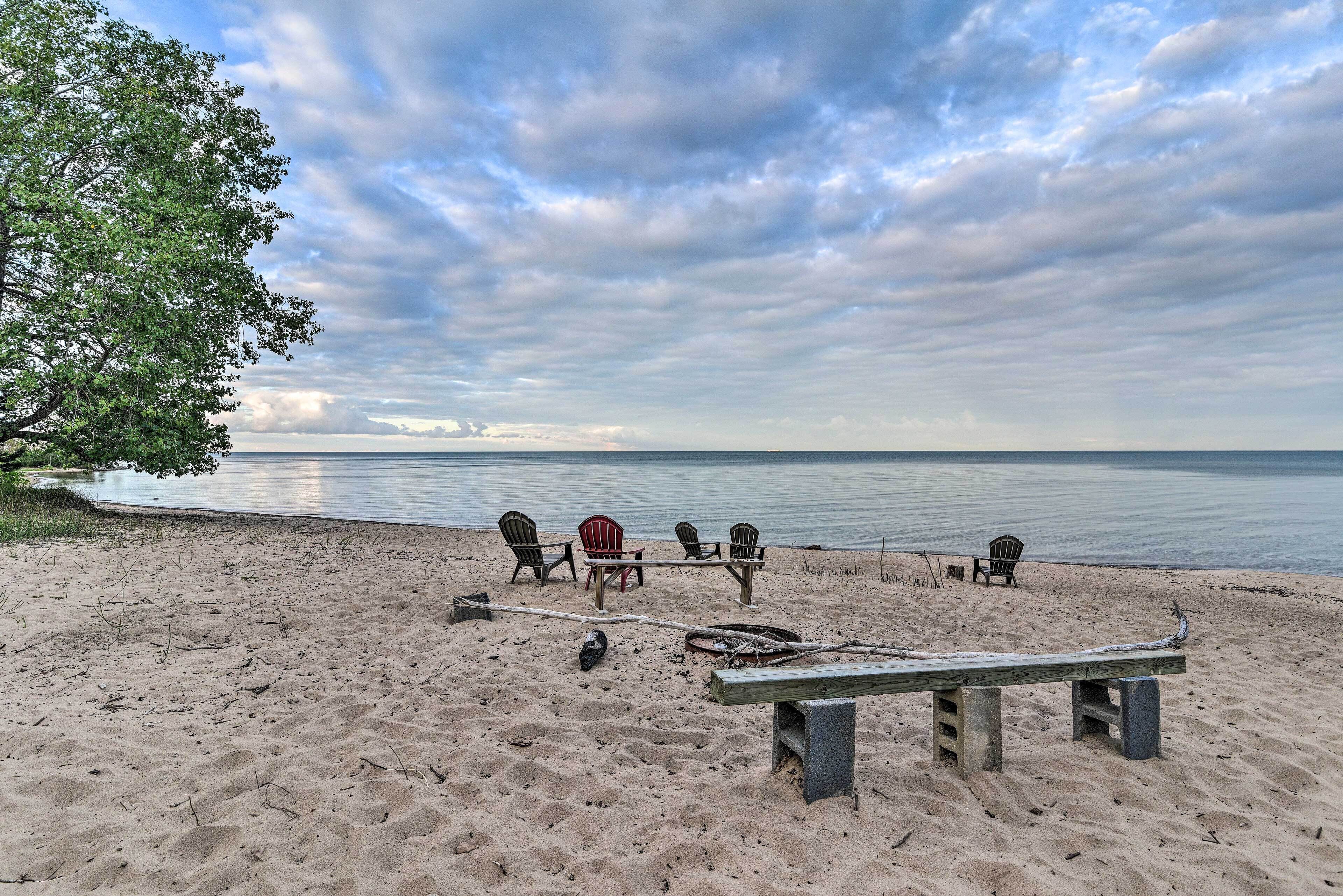 A beach with a wooden bench, four Adirondack chairs, and a table.
