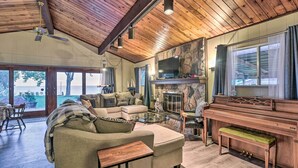 Un salón acogedor con techo de madera, chimenea, piano y televisor grande.