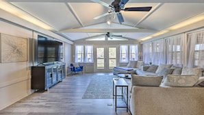Ein geräumiges Wohnzimmer mit hoher Decke, Deckenventilatoren, einem großen Fernseher und einer Sitzecke mit Sofas und Sesseln.