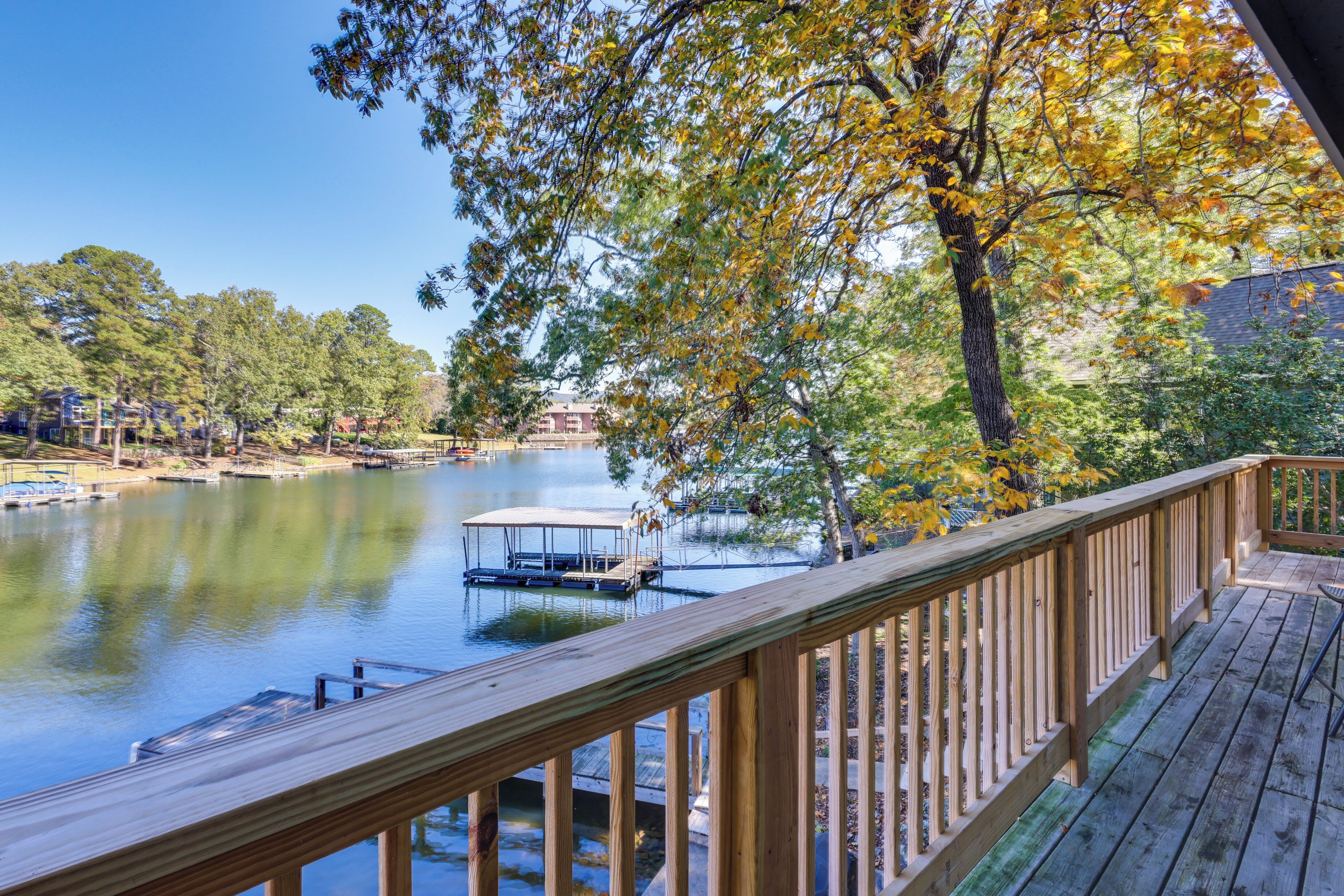 A wooden deck overlooking a calm lake with a dock and a covered seating area.