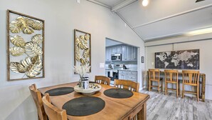 Ein Essbereich mit Holztisch und -stühlen, einer Wanddekoration und einer im Hintergrund sichtbaren Küche.