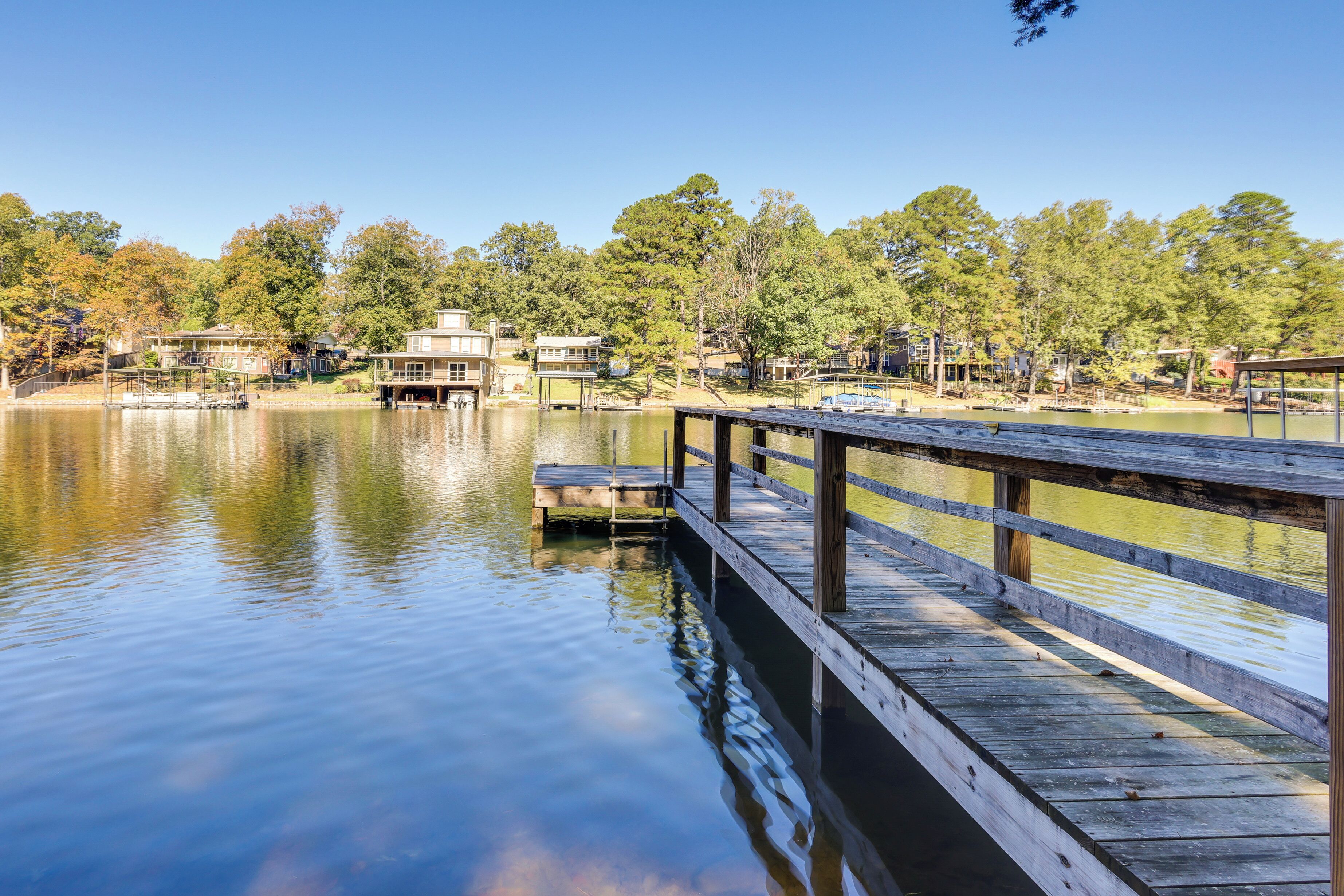 A wooden dock extending over calm water with a backdrop of trees and buildings.