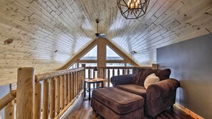 A cozy loft bedroom with a wooden ceiling, a large window, a wooden railing, and a brown sofa. - Lakefront Cottage in Iron River: 3 Mi to Skiing! (Iron River)