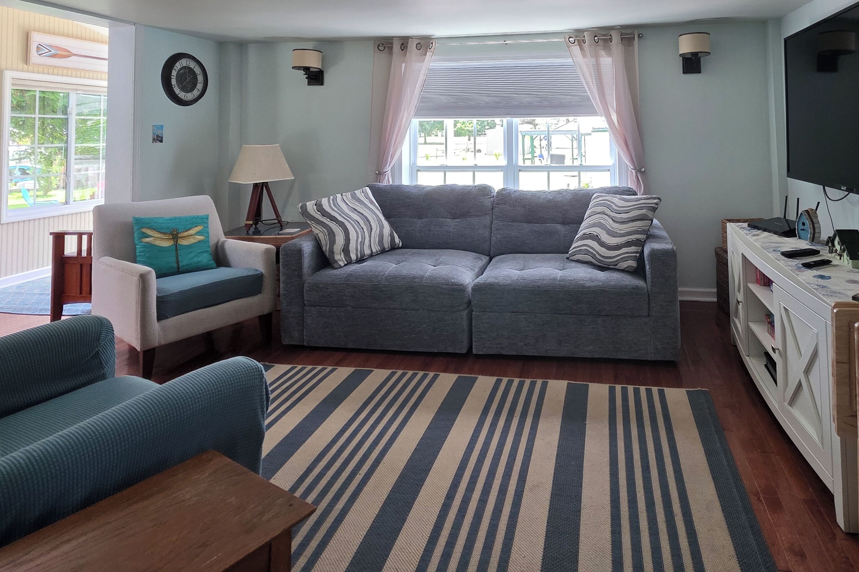 A living room with a grey sofa, a blue armchair, a wooden coffee table, a striped rug, a TV, and a lamp.