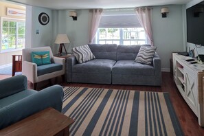 A living room with a grey sofa, a blue armchair, a wooden coffee table, a striped rug, a TV, and a lamp. - Lakeside Kent Home w/ Pier + Boat Ramp Access (Kent)