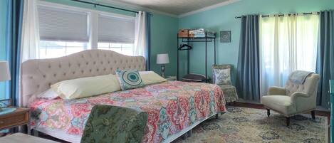 A bedroom with a large bed, a chair, a desk, and a ceiling fan.