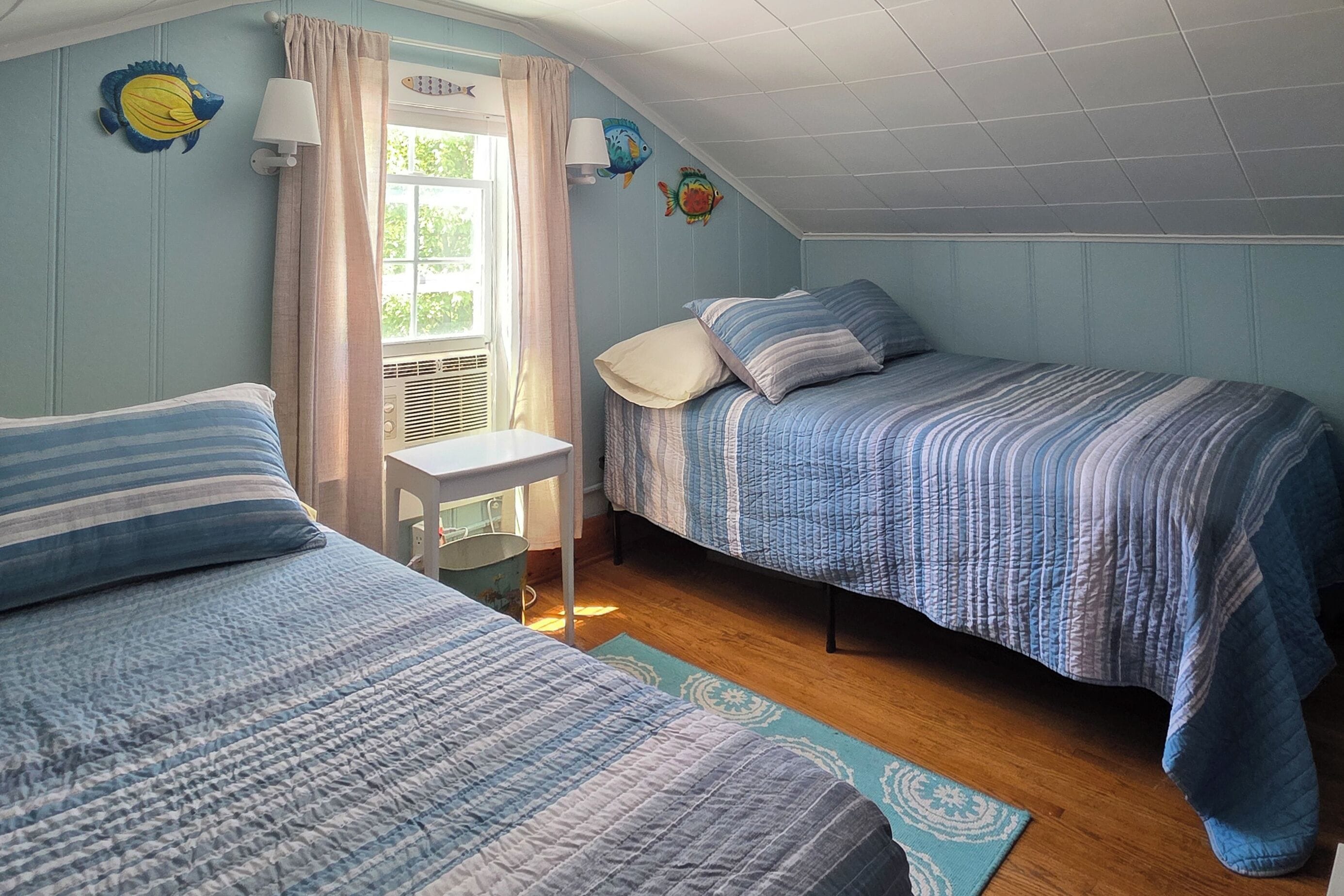 A room with two beds, a small table, a window with curtains, and wall decorations.