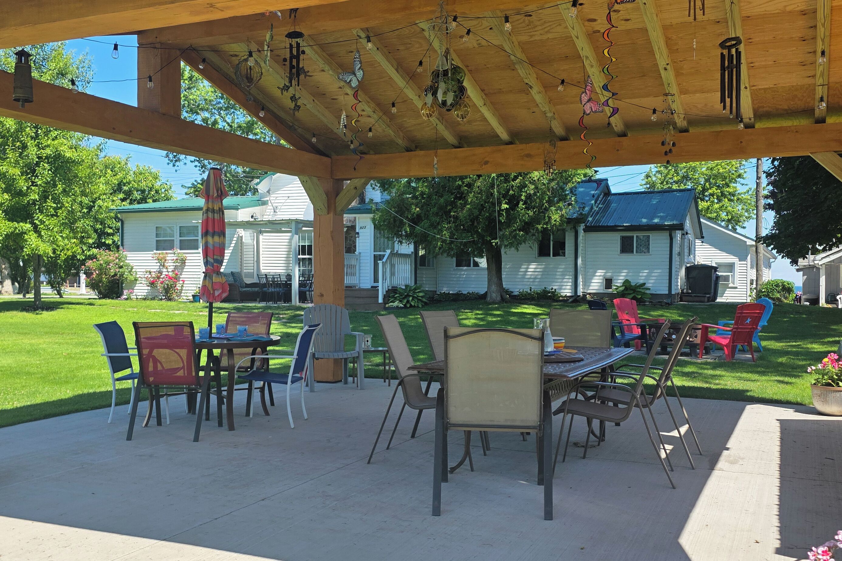 Un patio techado con mesas y sillas, una guirnalda de luces y vistas a casas al fondo.