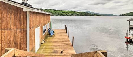 A wooden dock extending from a building with a view of a lake and distant hills.