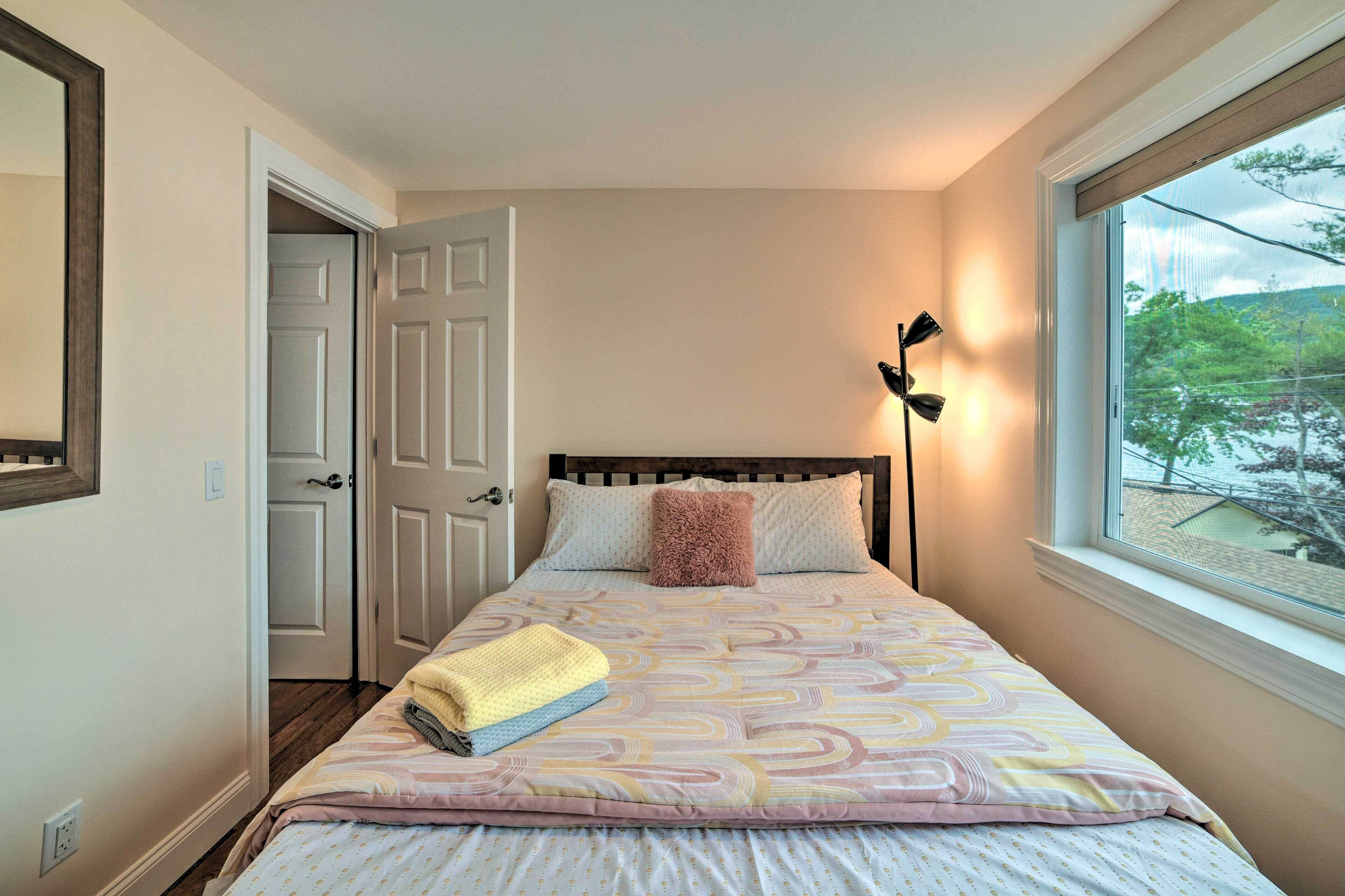 A bedroom with a bed, a window with a view, a door, and a lamp.