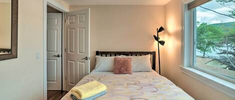 A bedroom with a bed, a window with a view, a door, and a lamp.
