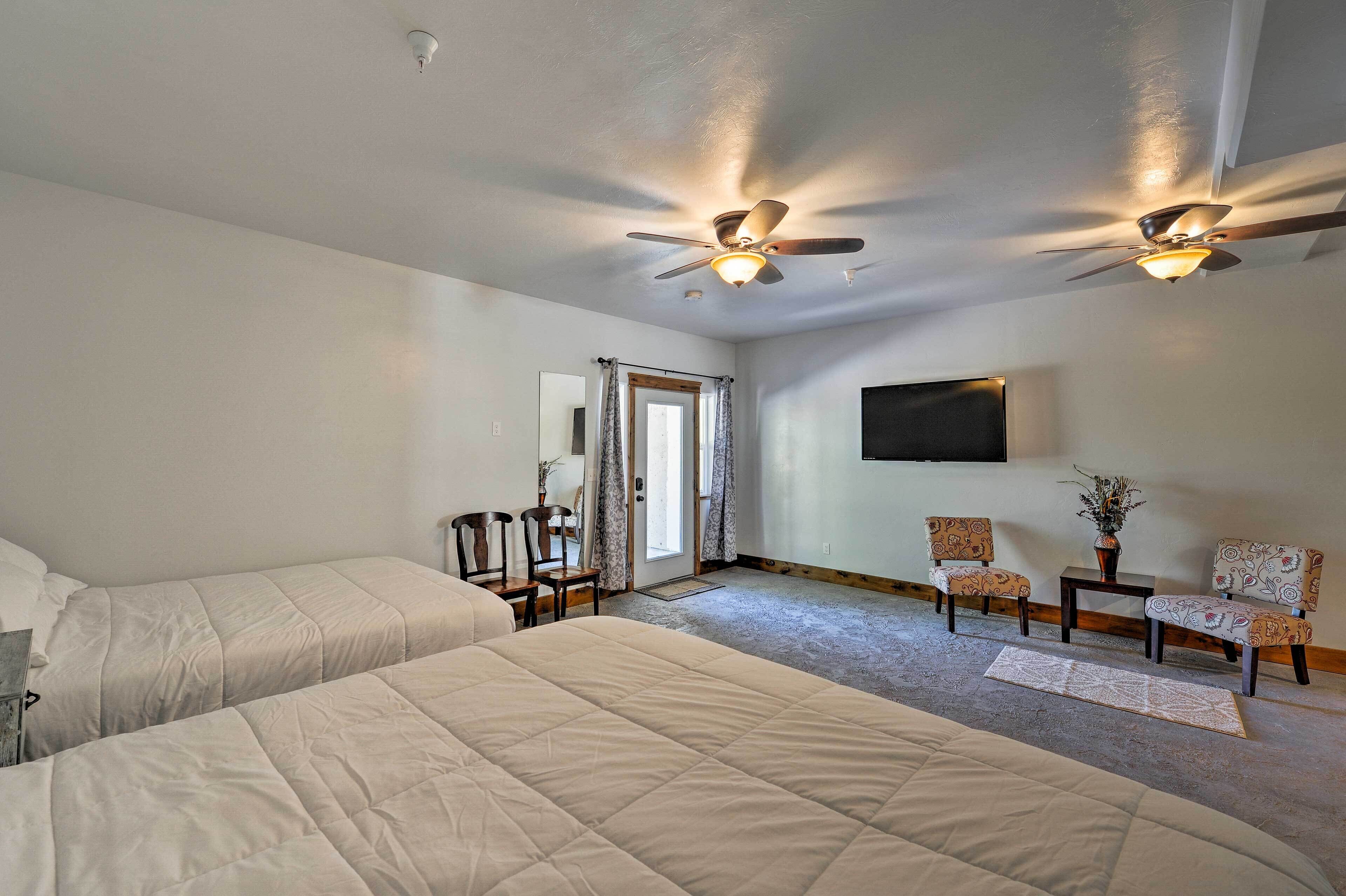 A hotel room with two beds, a ceiling fan, a flat-screen TV, and a small table with chairs.