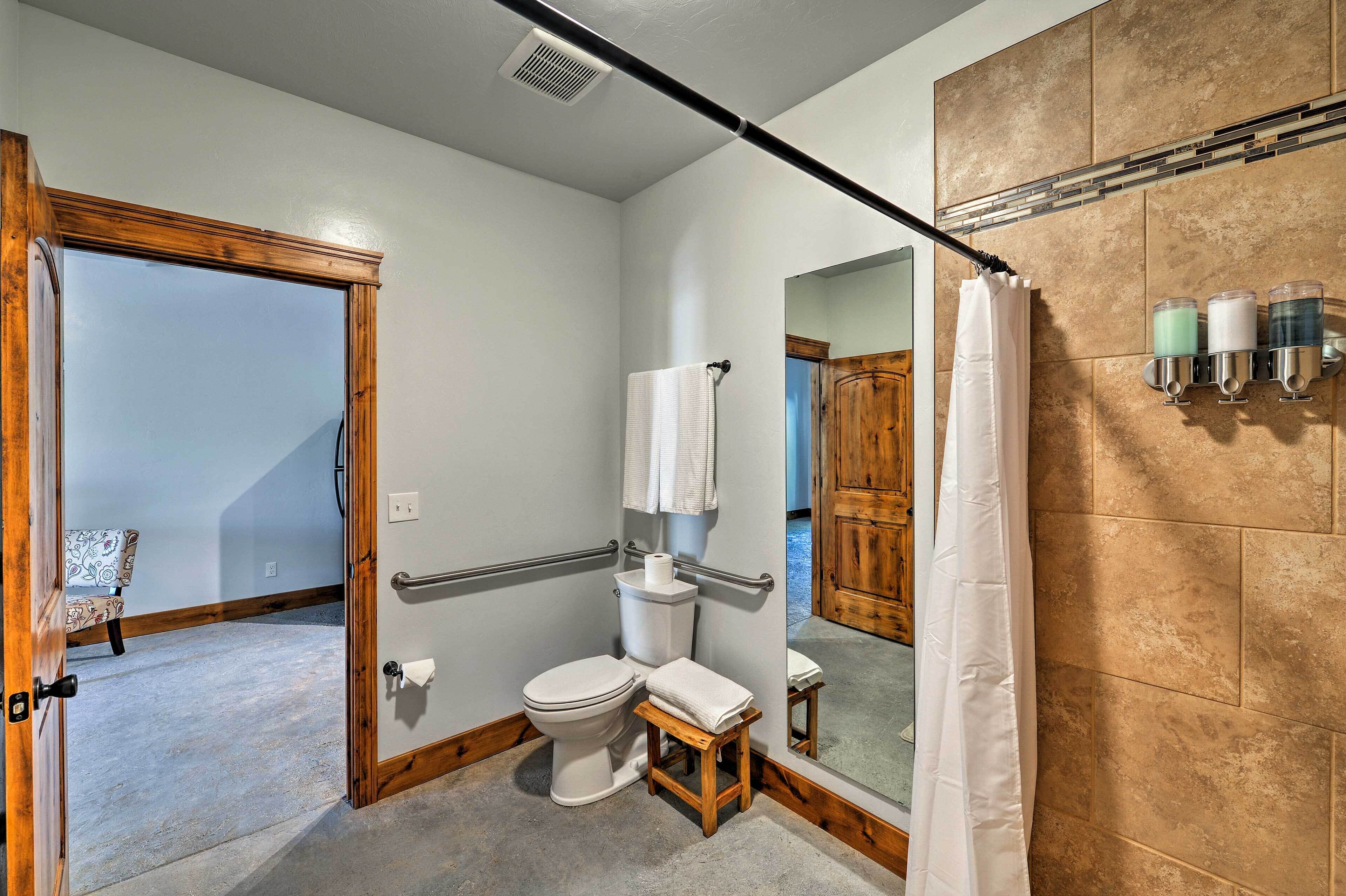 Un baño con inodoro, un taburete de madera, toallero, cortina de ducha y espejo.