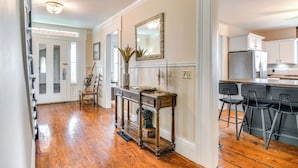 A hallway with a wooden floor leading to a kitchen area with a bar counter and stools.