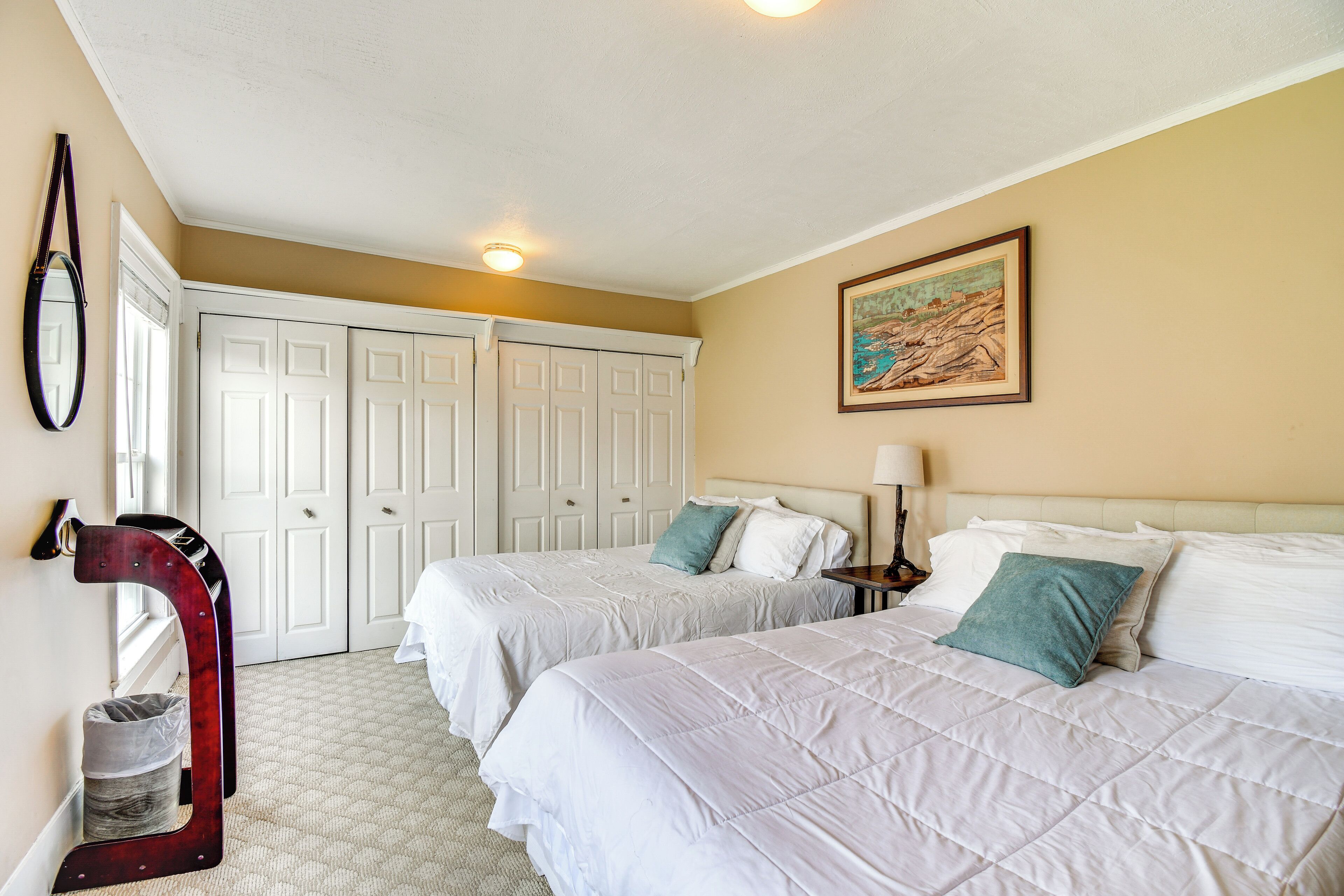 A hotel room with two beds, a large mirror, a painting on the wall, and a closet with white doors.