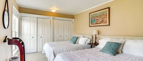 A hotel room with two beds, a large mirror, a painting on the wall, and a closet with white doors.