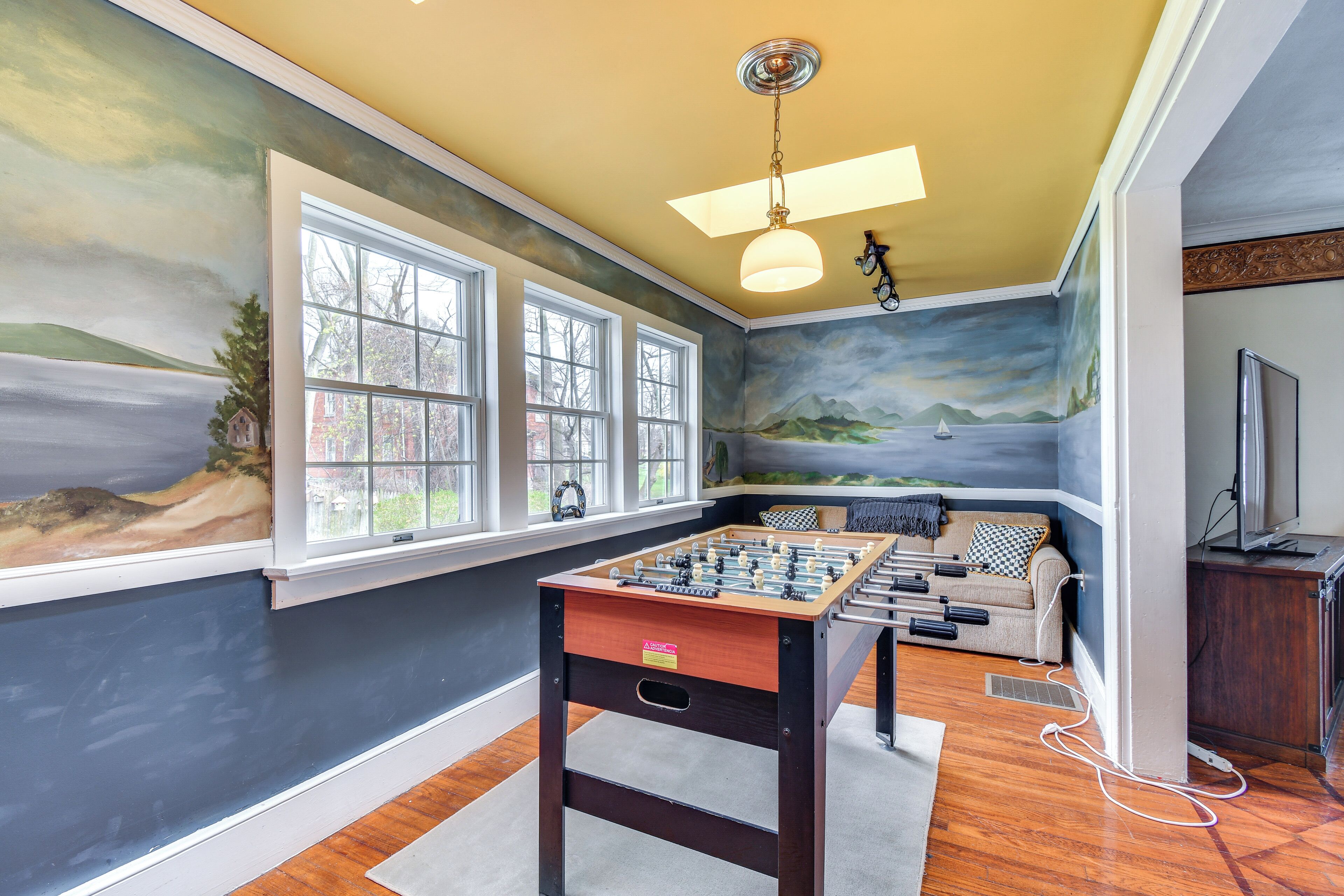 A room with a foosball table, large windows, and a mural of a landscape.