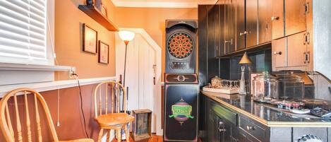 A compact kitchen with wooden cabinets, a dartboard, and a refrigerator with a Tournament Master logo.