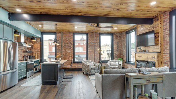 Une cuisine moderne avec un plafond en bois, de grandes fenêtres et un coin salon comprenant un canapé et des fauteuils.
