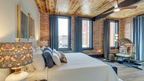 Une chambre avec un grand lit, un plafond en bois, des murs en briques et de grandes fenêtres.