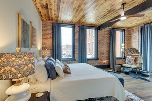 A bedroom with a large bed, a wooden ceiling, brick walls, and large windows. - Luxurious Downtown Murphy Vacation Rental Loft! (Murphy)