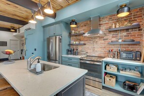 A modern kitchen with a central island, stainless steel appliances, and a brick accent wall. - Luxurious Downtown Murphy Vacation Rental Loft! (Murphy)