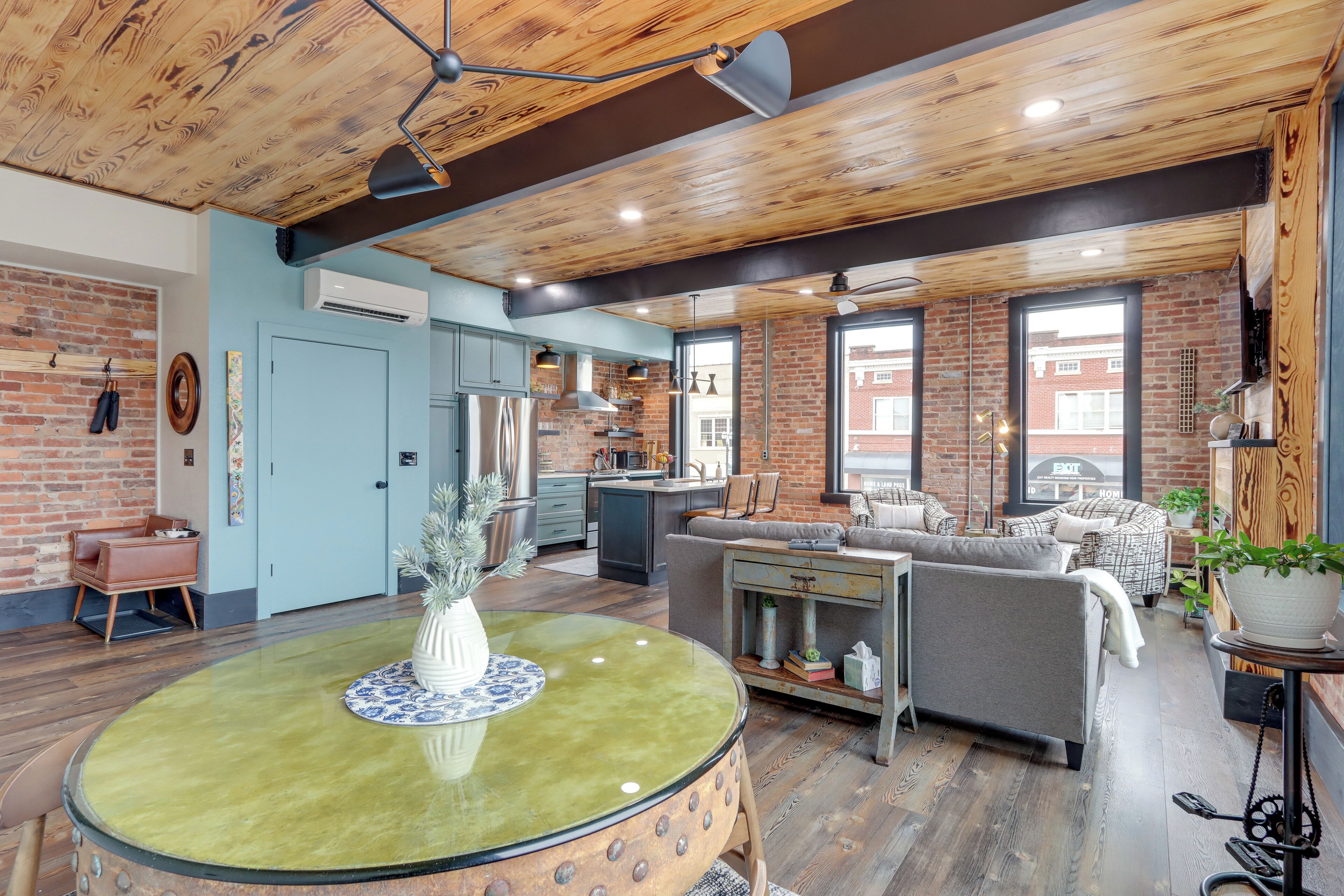 A modern kitchen with a brick wall, a dining area with a round table, and a living room with a sofa and a coffee table.