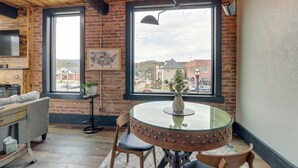 Une pièce chaleureuse avec une table ronde en verre, un canapé confortable et une grande fenêtre donnant sur des immeubles et une rue.