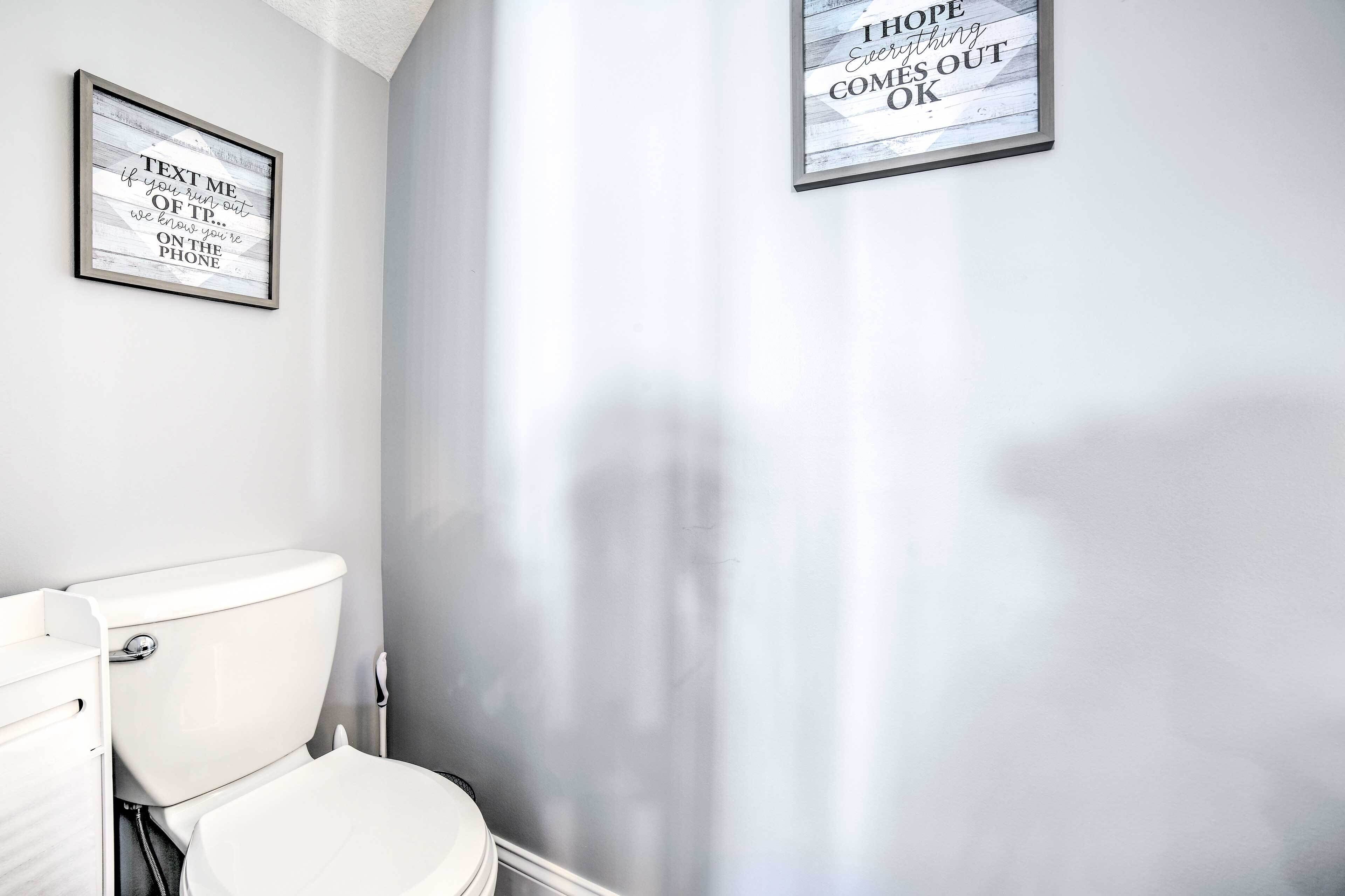 Een badkamer met een wit toilet, een raamdecoratie met een citaat aan de muur en een douchegordijn.