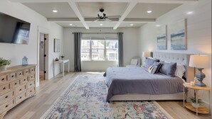 A bedroom with a bed, bedside tables, a ceiling fan, a TV, and a view of the outside.