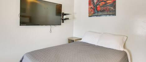 A bedroom with a bed, a mounted TV, a nightstand, and a painting on the wall.
