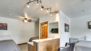 A bedroom with two beds, a wooden desk, a chair, a ceiling fan, and a mounted TV. - Lava Hot Springs Studio w/ Deck: Walk to Hot Pools (Lava Hot Springs)