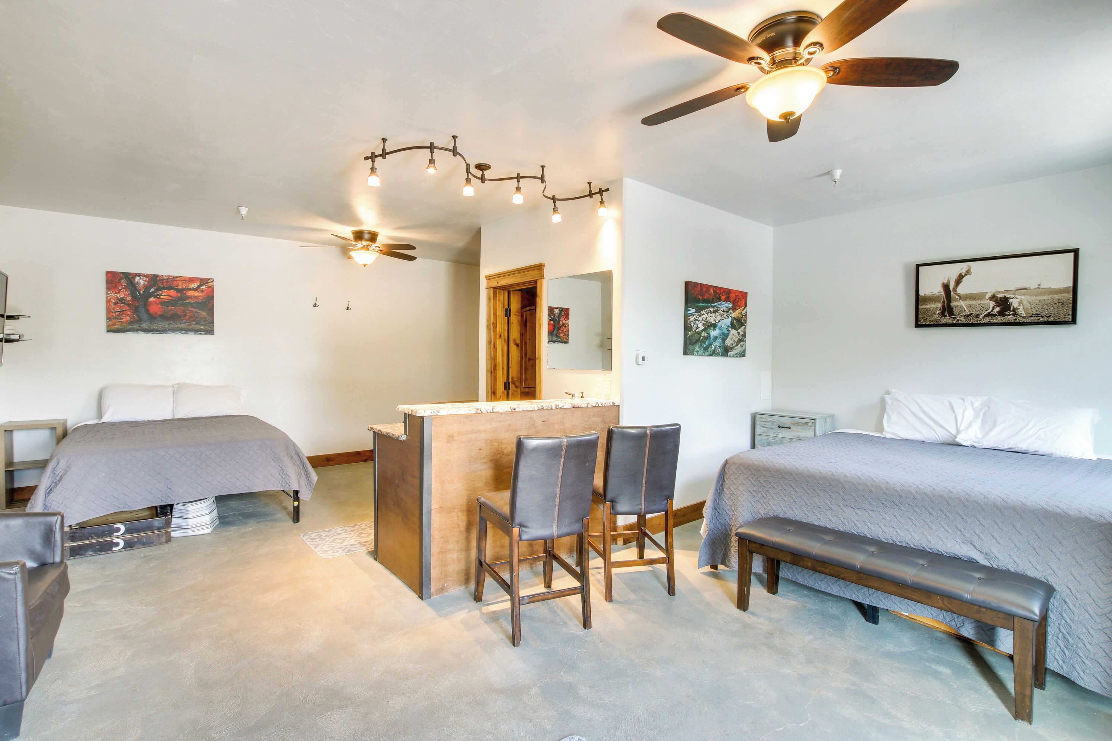 Ein Schlafzimmer mit einem Bett, einem Schreibtisch, zwei Stühlen, einer Bank, einem Deckenventilator und Kunstwerken an den Wänden.