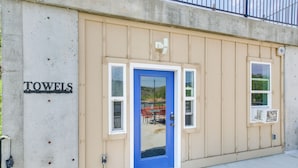 A building with a blue door, a sign reading "TOWELS", and a window with an air conditioning unit. - Lava Hot Springs Studio w/ Deck: Walk to Hot Pools (Lava Hot Springs)